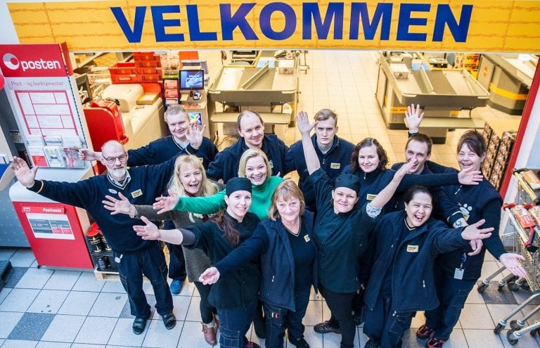 Happy personnel at Coop Prix Korgen standing eagerly below the entrance of the store that says “Welcome”.