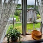 Nostalgic view from a bedroom at Inderdalen Farm, with old curtains in the window and view of the other farm buildings.