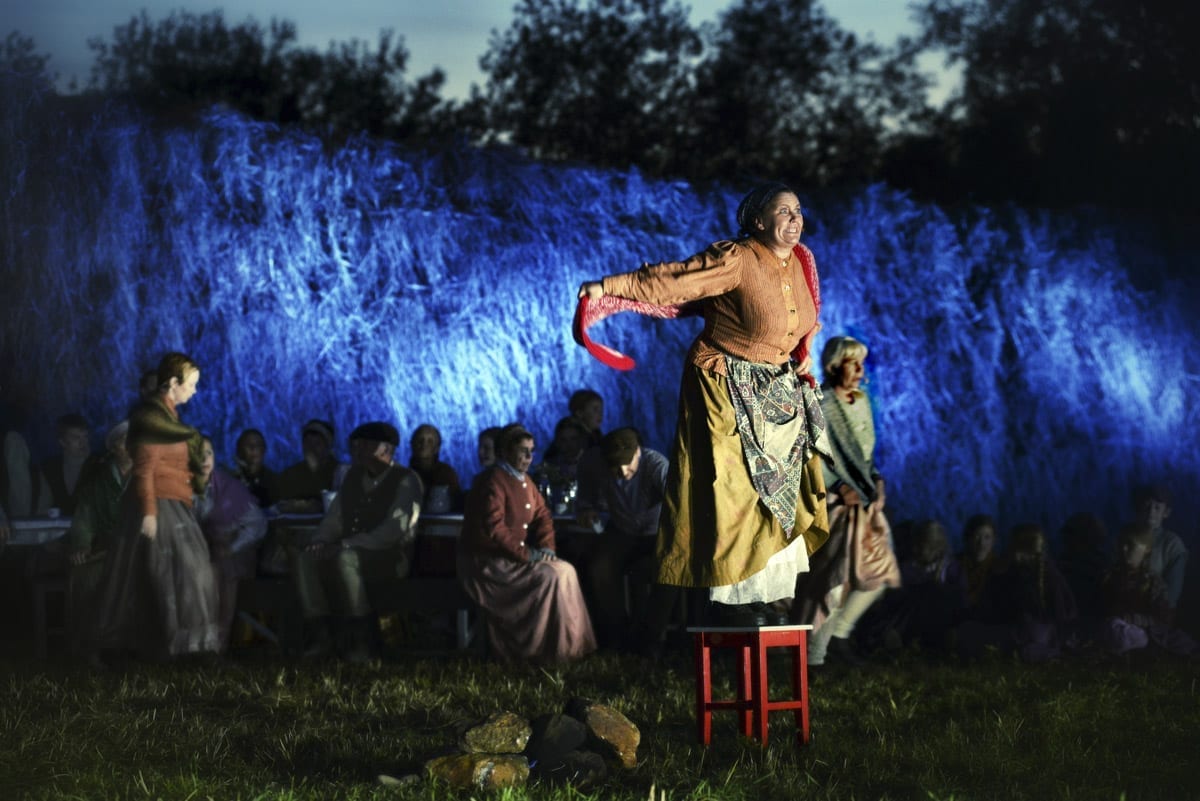 Woman dressed in an old costume standing on a chair and speaking eagerly, during the local play, Klemetspelet.