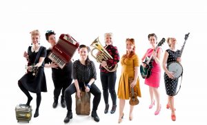 Band-picture of the seven happy and laughing women in Bitchy Big Boobies Bang Band holding their instrument.