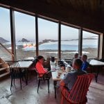 People eating in the dining room at Rabothytta, with big panorama windows showing the view over the glacier