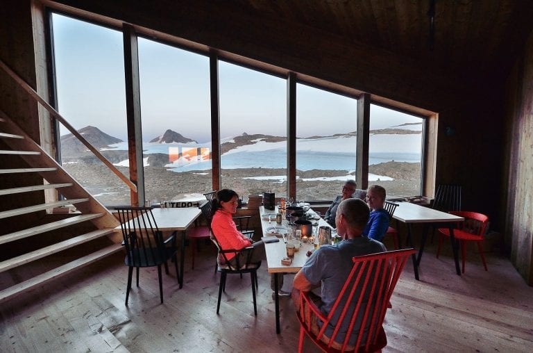 People eating in the dining room at Rabothytta, with big panorama windows showing the view over the glacier