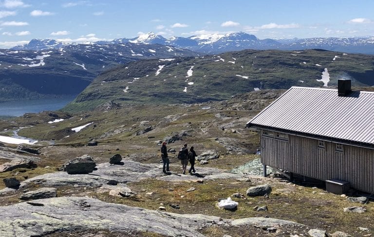 Hikers walking towards the cabin, Gråfjellhytta, during summer with a view over a big lake and more mountains in the horizon.