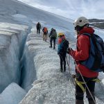 People walking with rope and crampons next to a huge crack in the glacier.