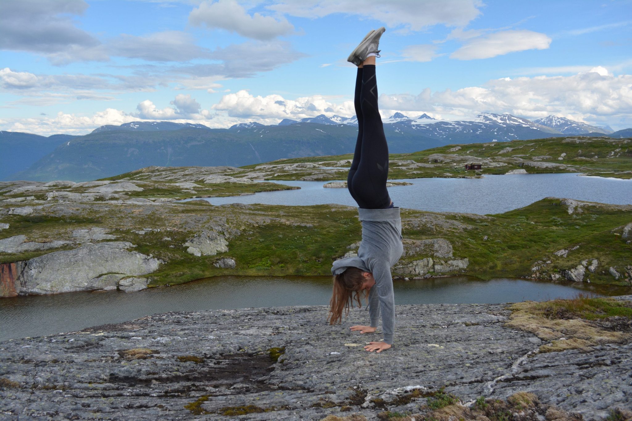Girl doing a handstand on a rocky peak in front of small lakes with the Okstindan-mountains in the background.