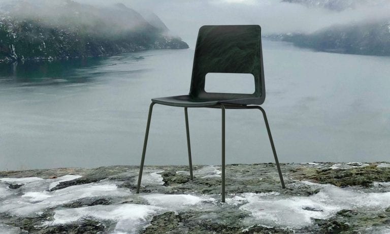 Black chair standing on a mountain rock in foggy surroundings, in front of the fjord and mountains around it.