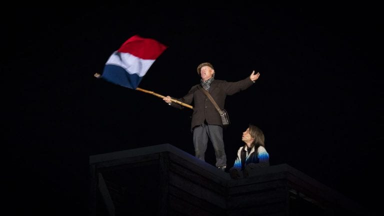 A man dressed in old local costumes, holding the flag of France in complete darkness, during the local play, Klemetspelet.