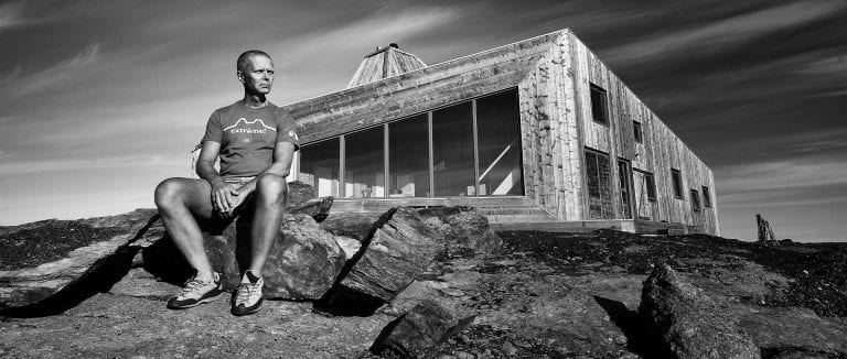 Black-and-white photo of Svein Arne, father of the cabin “Rabothytta” sitting on a rock in front of his cabin.