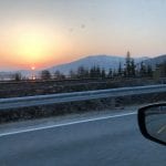 Beautiful red sun setting behind great mountains, seen from a car on the road.