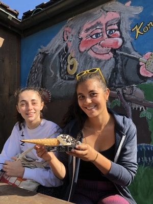Two smiling girls with an ice cream, sitting in front of a painting of a happy Norwegian troll at Korgfjellet Fjellstue.