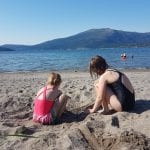 A typical summer day at Røssåauren with children building sandcastles in the sand while others are swimming in the fjord.