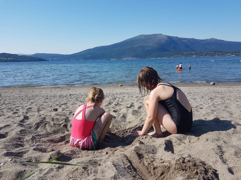 A typical summer day at Røssåauren with children building sandcastles in the sand while others are swimming in the fjord.