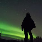 Person overlooking the northern lights on a starlit sky