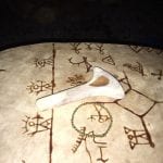 Sami drum covered with sami pictograms and a sami-hammer laying on top of the drum ready to be played.