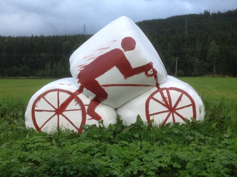 White silage bales standing on an acre, painted with a red cyclist as decoration for “Artic Race” in 2016.