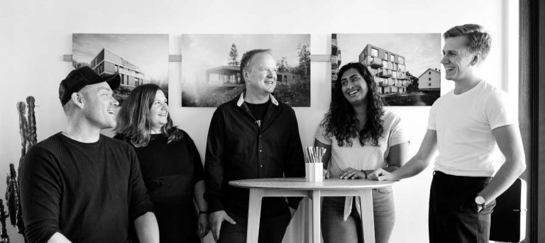 Black-white photo of the people behind “Tanken arkitektur”, in their studio with some of the designs illustrated behind them.