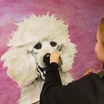 Young girl drawing a happy and fluffy white dog on a pink background, on a big canvas.