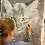 Young girl drawing a grey cat on a big canvas.