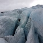 Brave person climbing up from one of many dark cracks in the ice blue glacier.