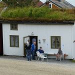 People going in and out of a small white wooden house with grass on the roof, the Gunvor House at Lapphella.